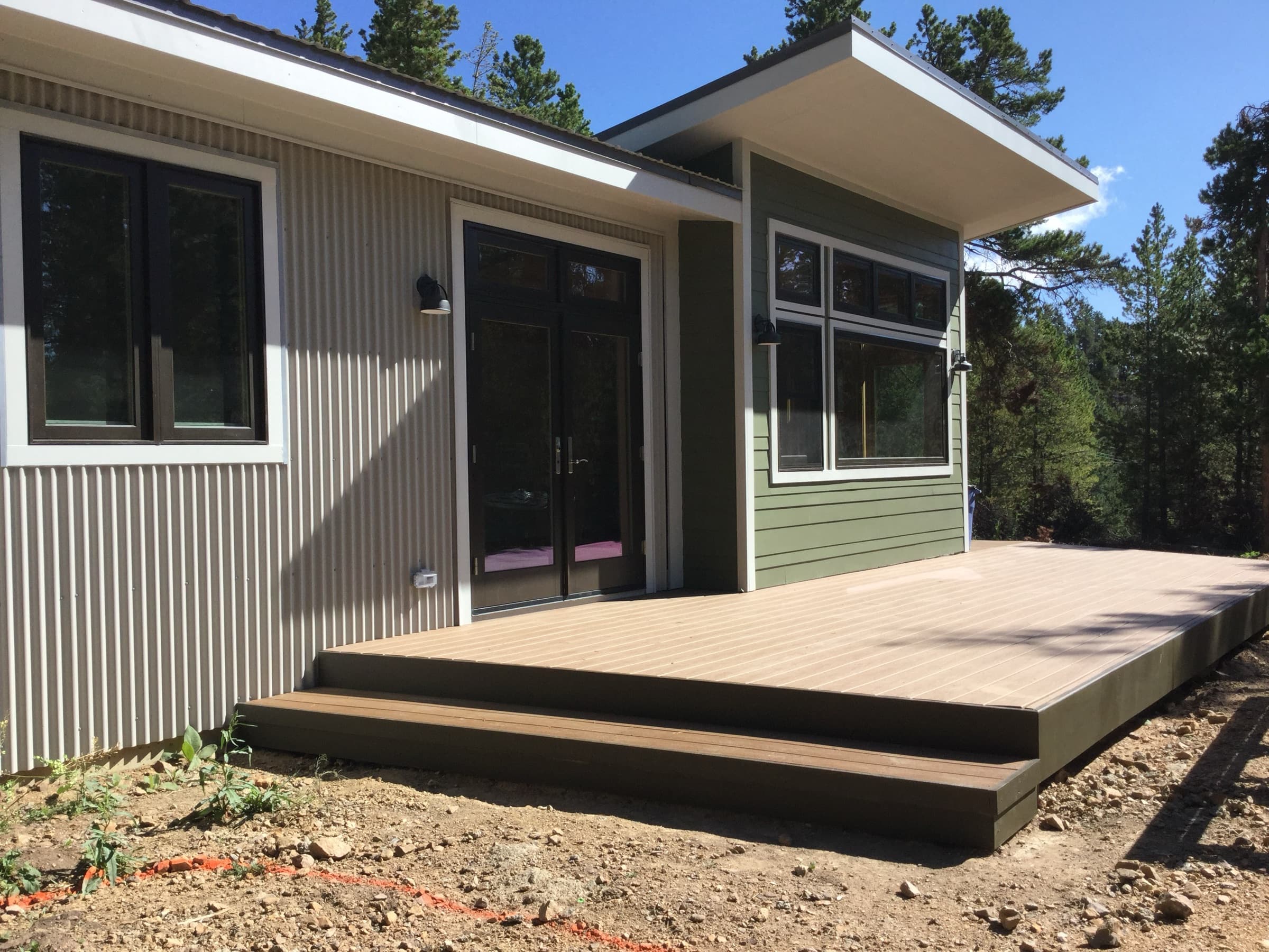 Cabin deck with glass doors, mixed siding, and a forest backdrop