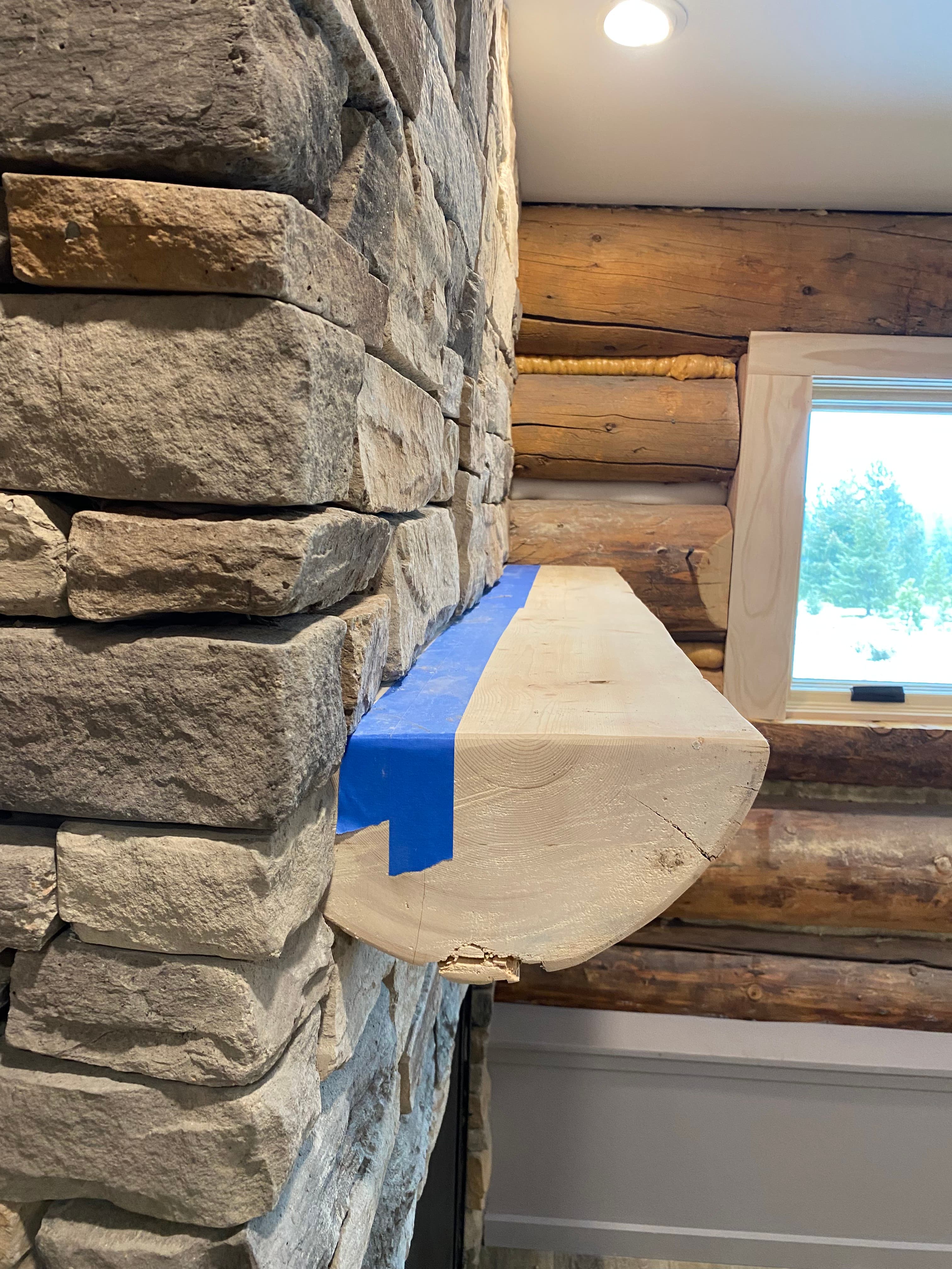 Close view of a split-log mantel set into stacked stone, with a log wall and window beyond