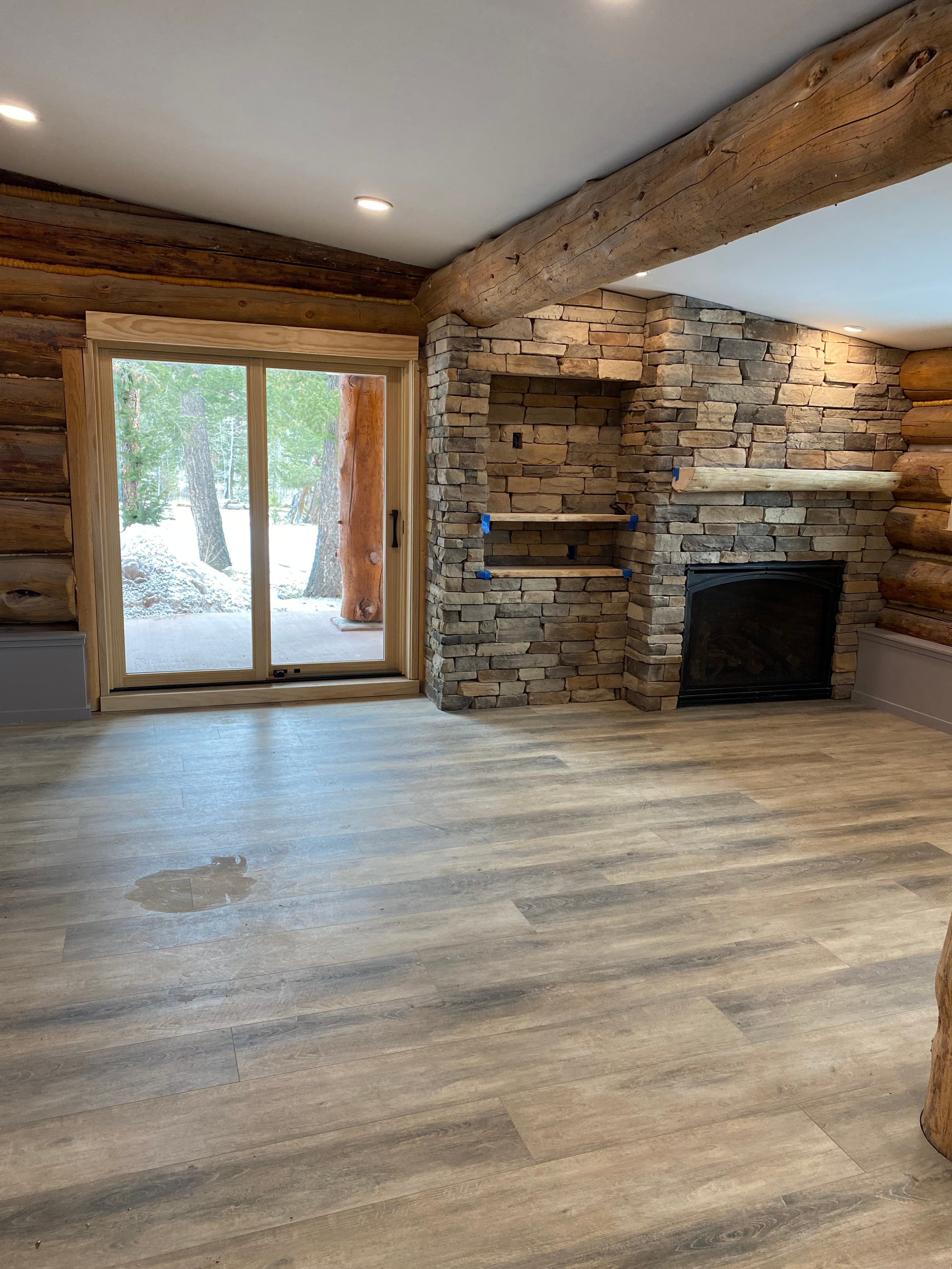 Cabin room with stacked-stone fireplace, log walls, plank floors, and a sliding door to snow