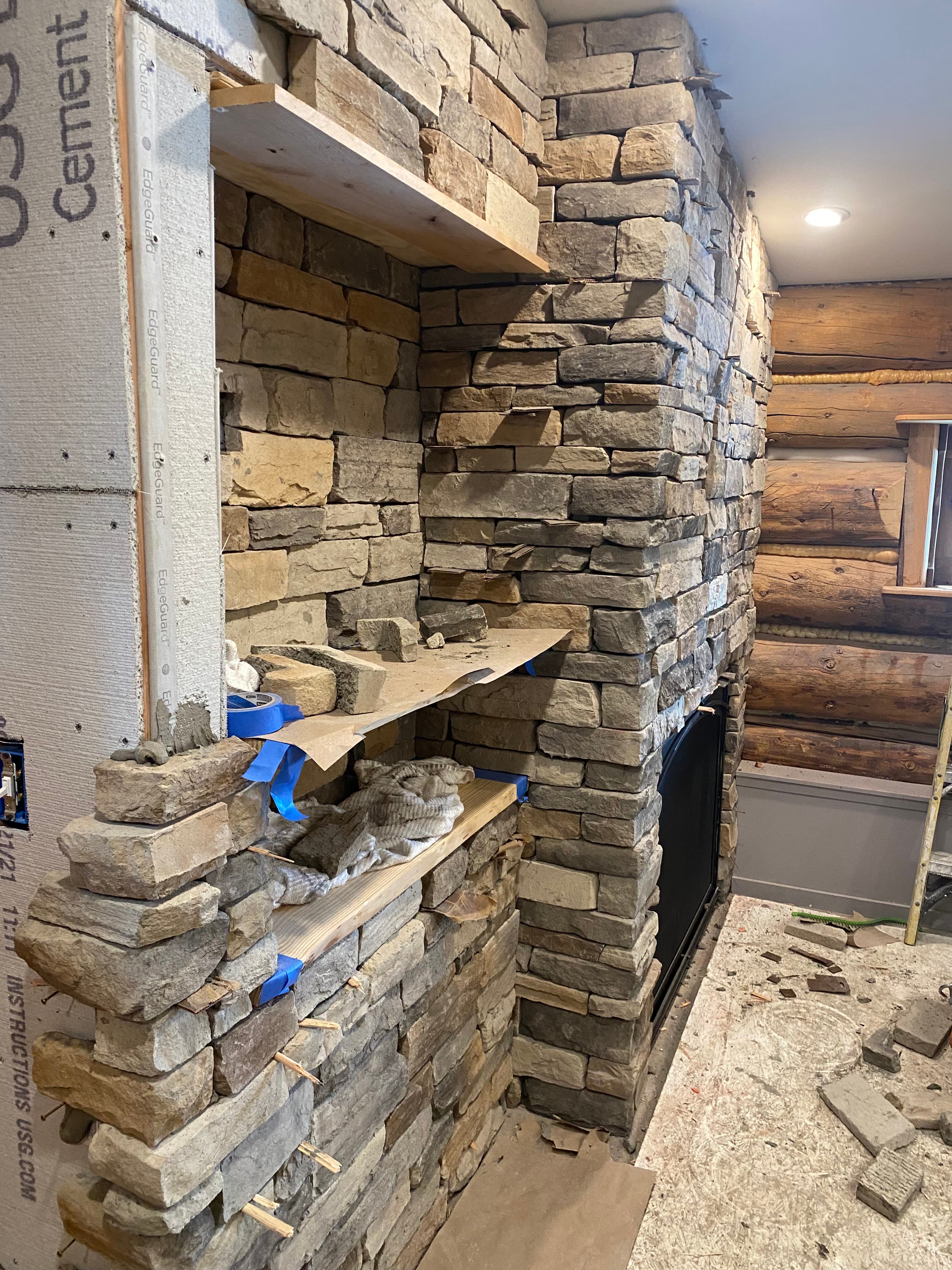 Close view of stacked tan and grey stone around a fireplace insert and recessed shelves