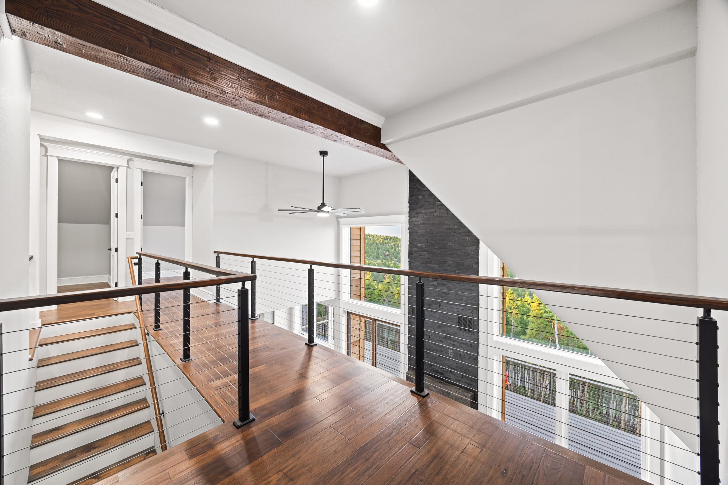 Upper catwalk with cable rail looking into the vaulted great room and stone fireplace