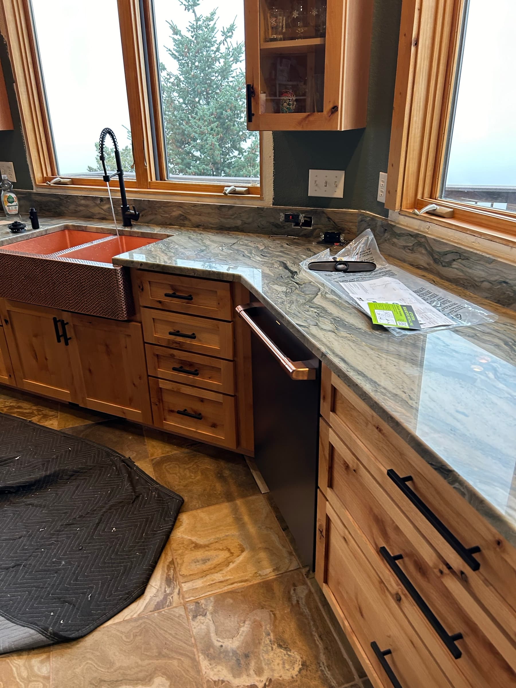 Hammered copper farmhouse sink and black faucet under wood-framed windows