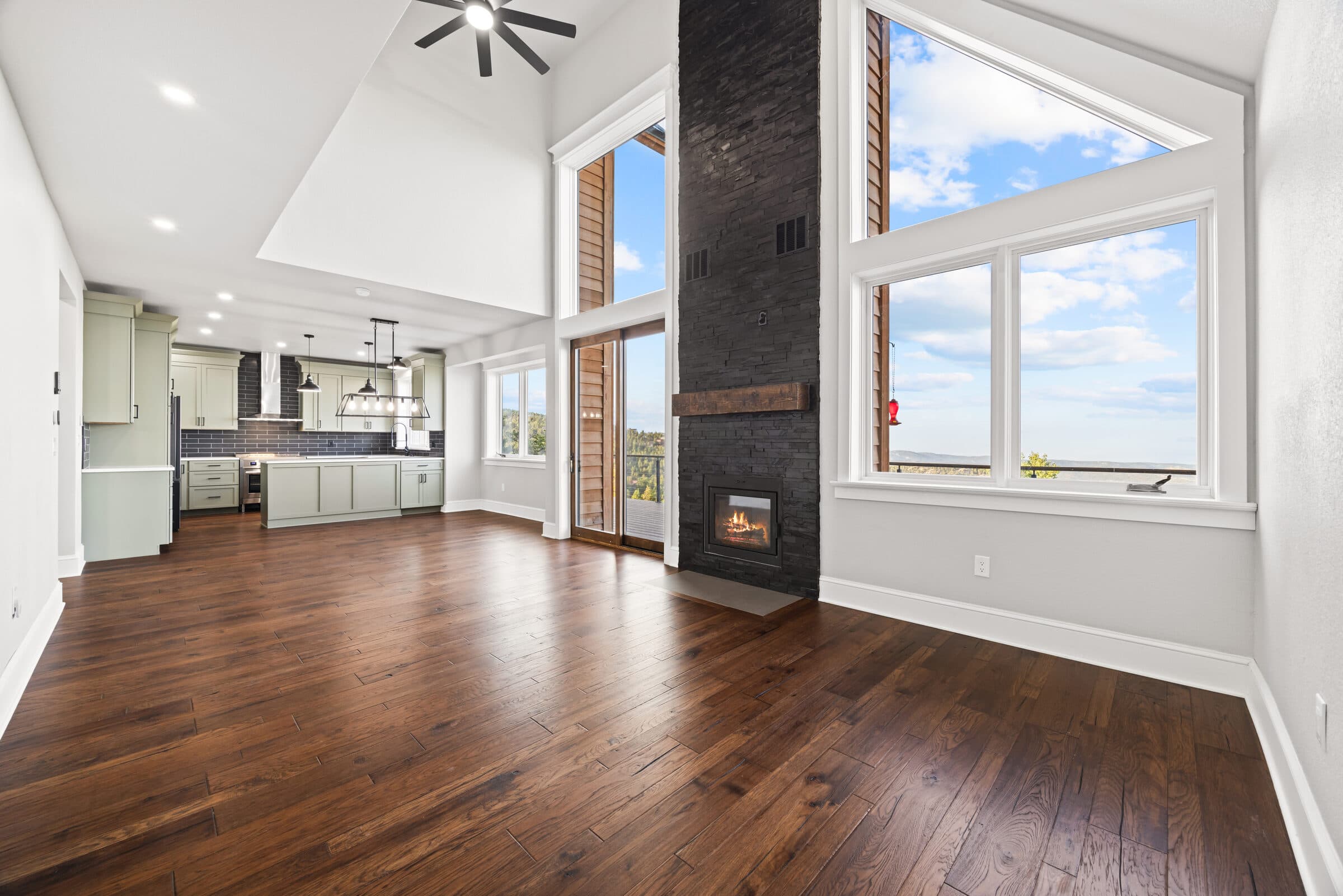 Vaulted great room with a floor-to-ceiling stone fireplace and a sage kitchen beyond