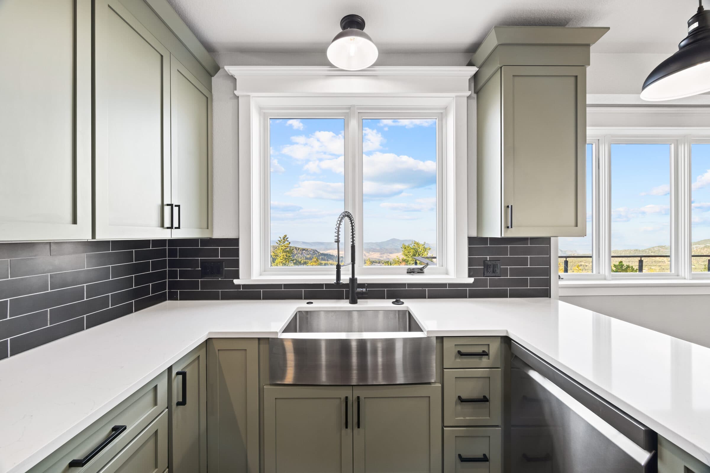 Farmhouse sink and black faucet under a window, with sage cabinets and dark subway tile