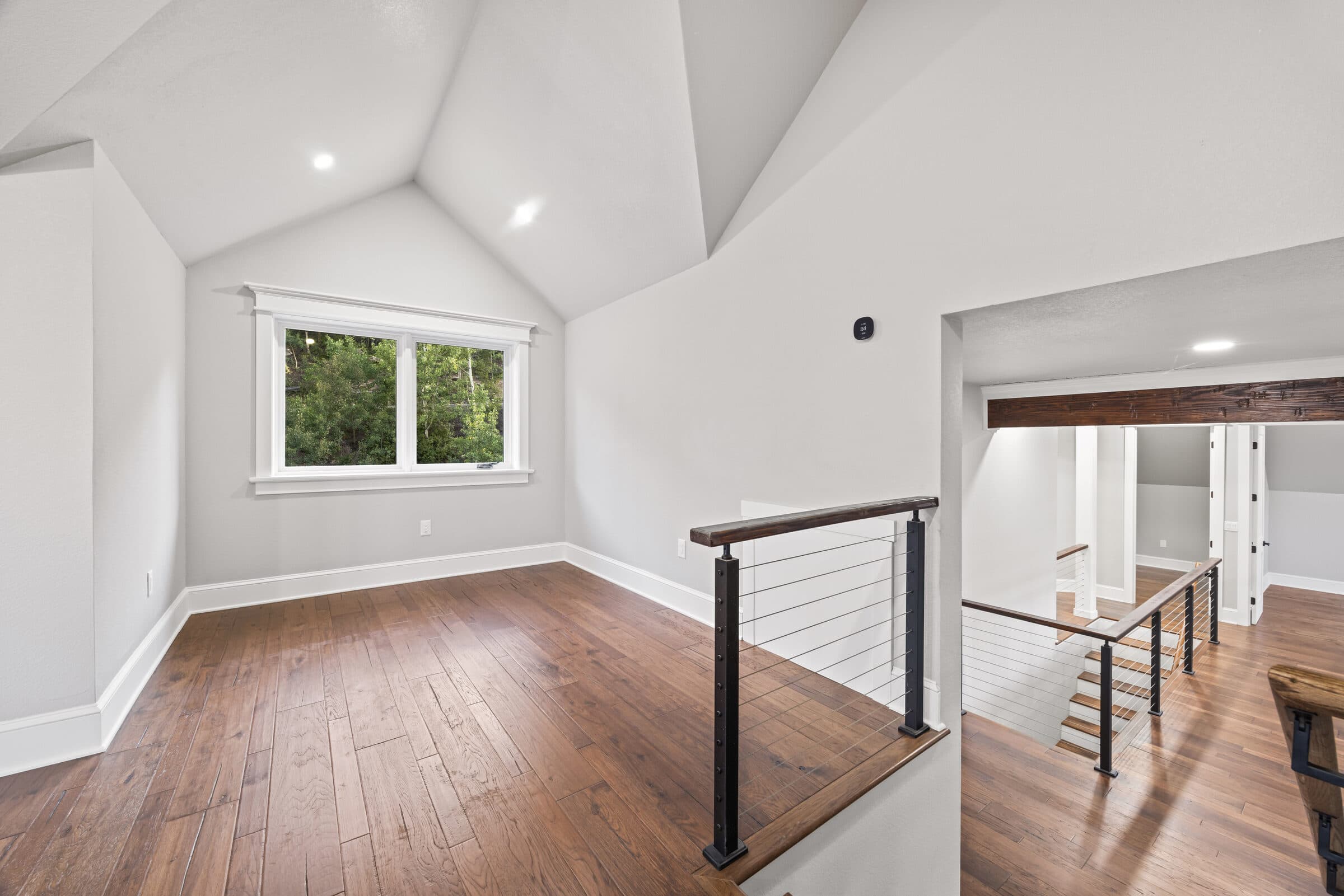 Loft with vaulted ceiling, hardwood floor, and a cable rail at the stair