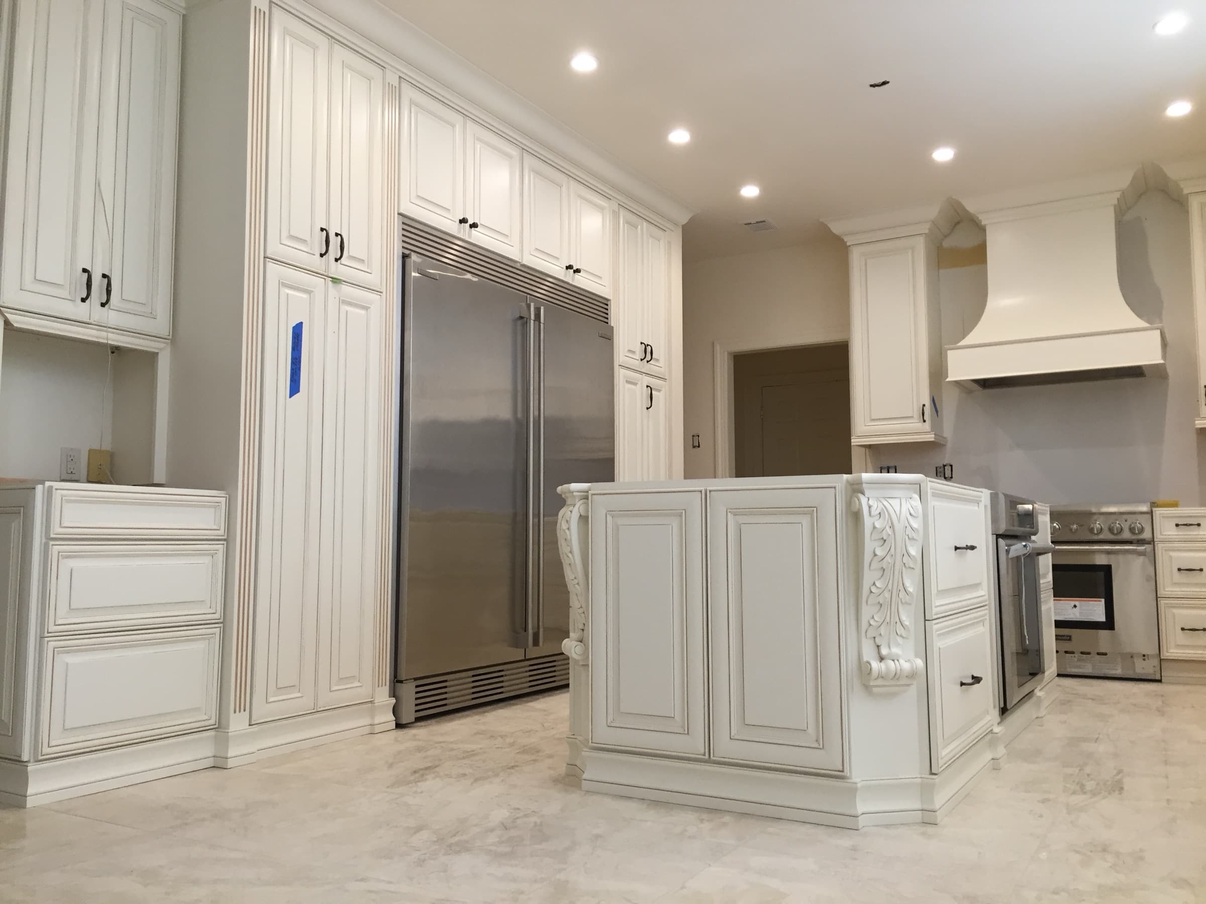 Wide view of the white kitchen cabinetry and carved island before counters