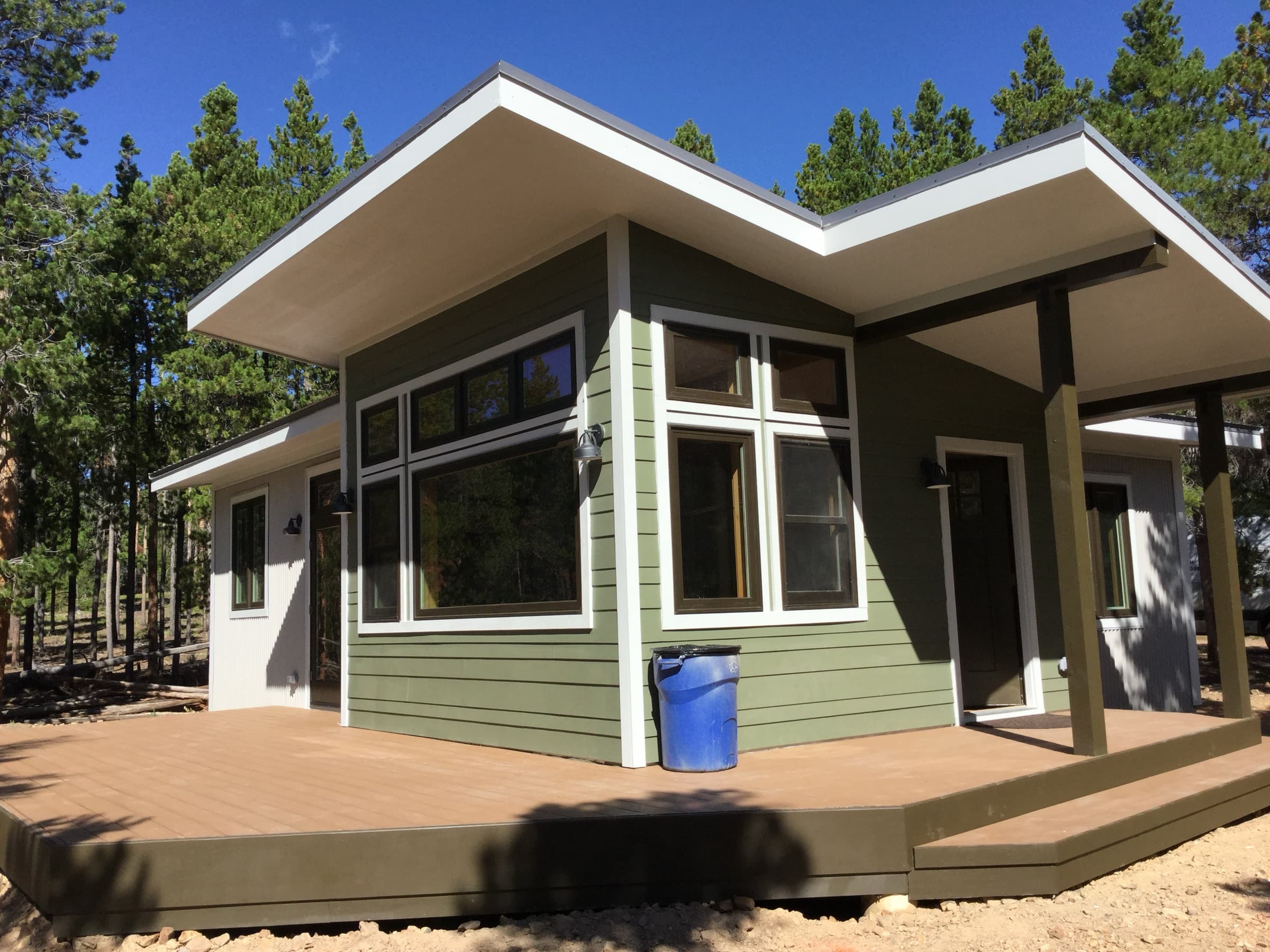 Finished shed-roof cabin with green siding, white eaves, and a wood deck in the pines