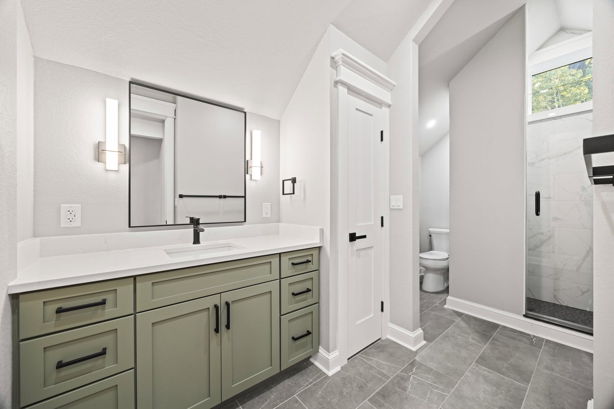 Sage bathroom vanity with a white counter, black faucet, and framed mirror