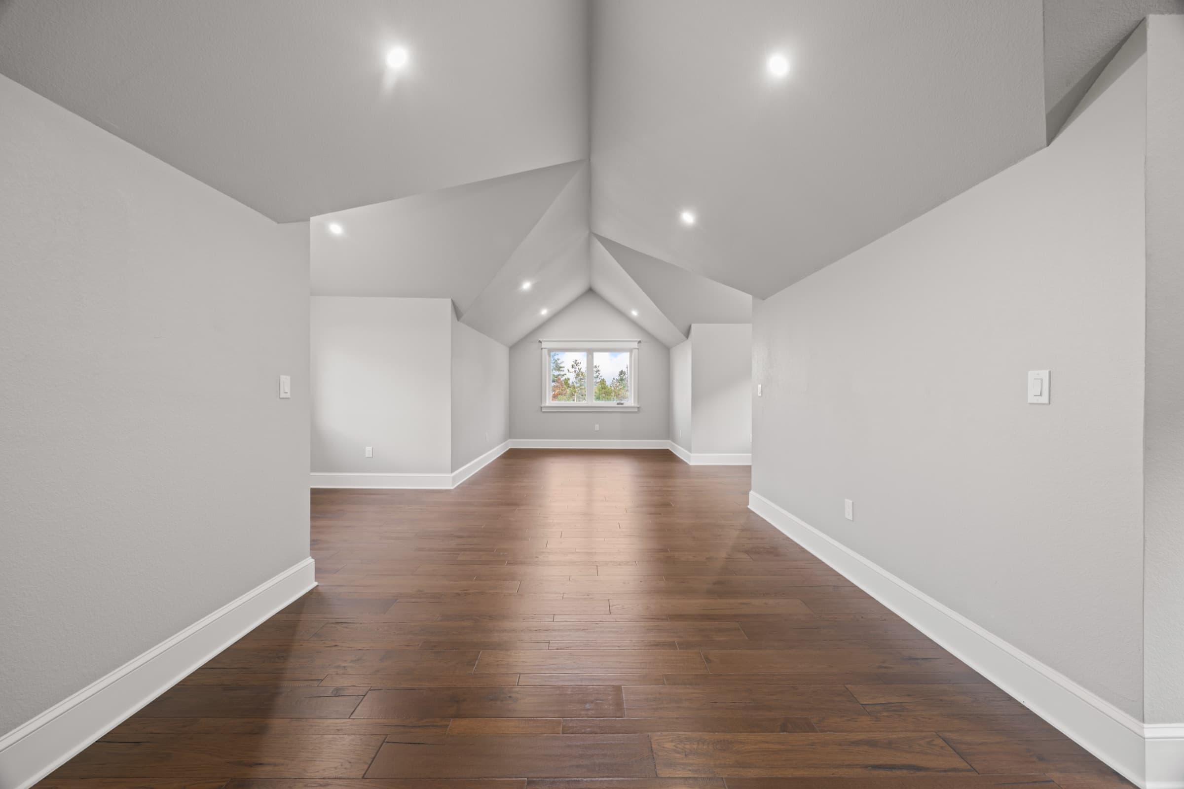 Finished upper room with a vaulted ceiling, dark hardwood floor, and a window into the trees