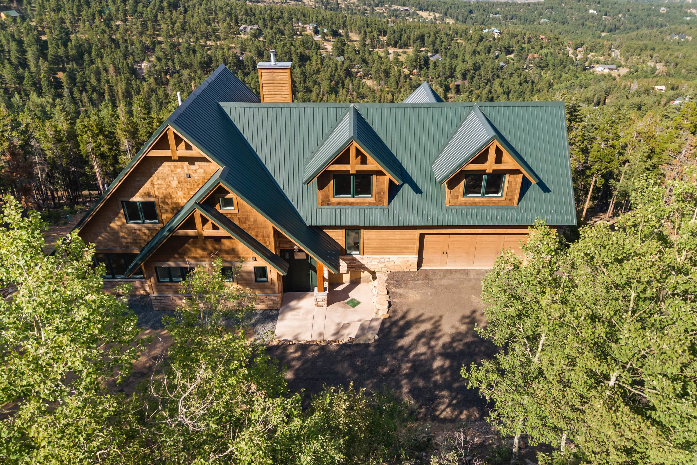 Custom house with a green metal roof, timber gables, wood siding, and a stone foundation